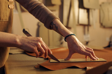 Artisan carefully cutting leather with sharp tool, focusing on detailed work. Engaging in precise manual process within well-organized workspace
