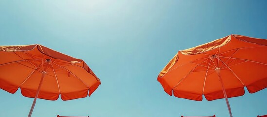 Beach chairs and vibrant orange umbrellas under a clear blue sky ideal for summer vacation concepts with space for personalized text