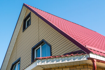 A newly built two-storey house with a metal roof.  The roof is made of metal tiles. Protection of the house from atmospheric precipitation.