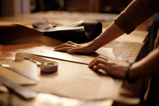 Person carefully working on leather crafts with precision equipment on wooden workbench, creating custom leather items in detailed craftsmanship process