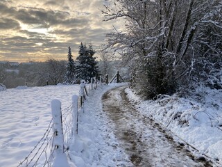 Friedvolle Landschaft in der Natur mit Weg und Weidezaun bei Sonnenaufgang im Winter mit Schnee