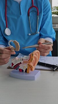 Closeup of hearing aid in audiologist hand near anatomical model of human ear