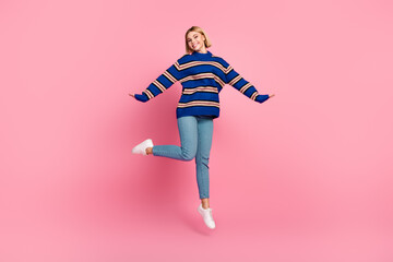 Fototapeta premium Happy woman jumping cheerfully in casual attire against a vibrant pink background showcasing an enthusiastic gesture