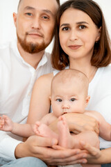 mom, dad with a baby, an international family, a Caucasian mom with an Asian husband and a baby in her arms in the bedroom gently hugs the baby holding in her arms, a place for text