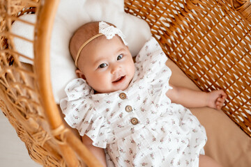 Asian baby girl in a wicker crib goes to bed, a small child smiles or laughs