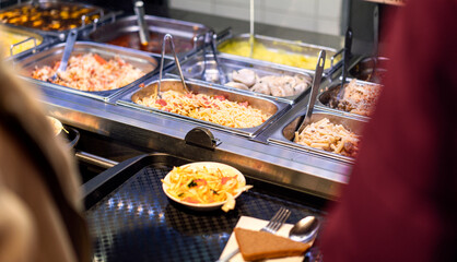 Heated buffet trays displaying prepared meals, stainless steel serving station with tongs, professional catering setup during lunch service