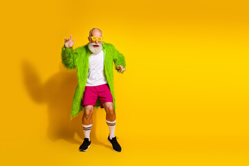 Charismatic elderly man posing stylishly in vibrant green coat and retro sportswear on yellow background