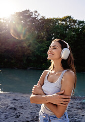 Young smiling woman with headphones enjoying healing music and sun embracing herself 