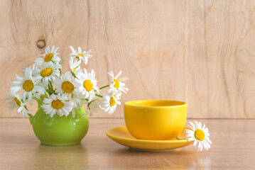 Summer breakfast: yellow cup of coffee or tea and bouquet of white daisies flowers on wooden table