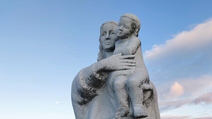 Statue of the Virgin Mary embracing a child against a blue sky