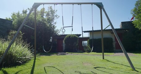 Empty children's playground at the backyard with swing swinging during sunny daytime. 