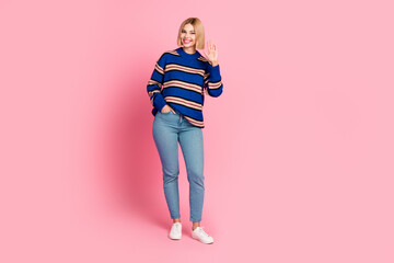Young woman in casual striped sweater posing with a cheerful wave on a pink background