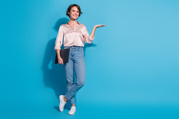 Young woman in satin blouse poses with confident gesture, holding document against blue backdrop