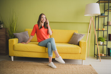 Obraz premium Full body photo of nice young girl sit sofa touch hair wear orange clothes enjoy modern bright cozy spring interior flat indoors