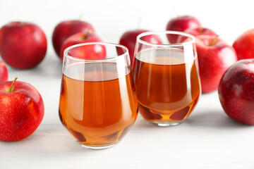 Fresh apple juice in glasses and fruits on white wooden table, closeup