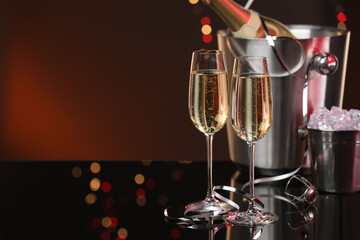 Champagne in glasses, bottle and ice buckets on mirror surface against color background with blurred lights, space for text