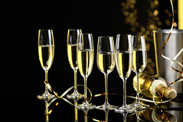 Champagne in glasses and bottle on mirror surface against black background with blurred lights