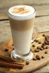 Tasty latte macchiato in glass cup, coffee beans and cinnamon on wooden table, closeup