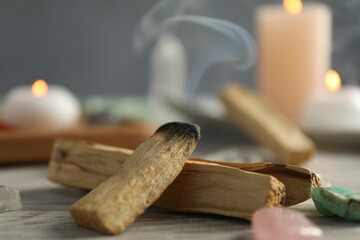 Smoldering palo santo stick and gemstones on wooden table, closeup