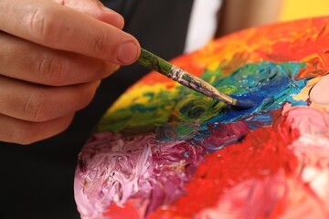 Man with paintbrush mixing paints on palette, closeup