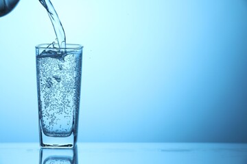 Pouring soda water into glass on light blue background, closeup. Space for text