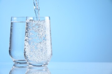 Pouring refreshing soda water into glasses on light blue background, closeup. Space for text
