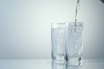 Pouring refreshing soda water into glasses on light grey background, closeup. Space for text