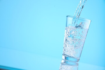 Pouring refreshing soda water into glass on light blue background, closeup. Space for text