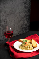Noodles served with garlic bread on a white plate, accompanied by a glass of red wine, all placed on a red cloth with a black sofa in the background for contrast.