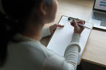 Reviewing Information on a Laptop Screen. Asian woman focused on reviewing charts on a laptop in a modern office environment.