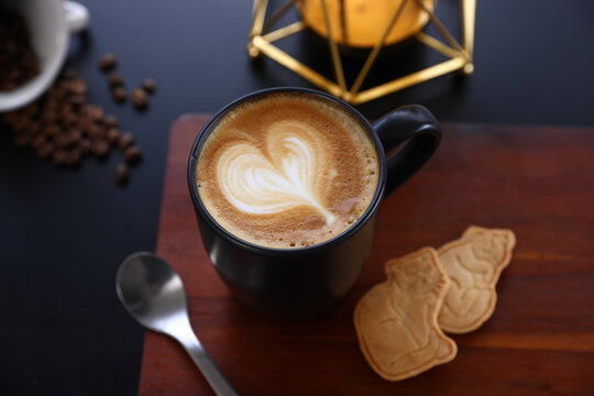 Hot Cappuccino coffee with black cup on old wooden table with isolate in black background