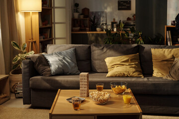 Group of cushions on grey comfortable couch standing in front of table with board game, drinks and snacks