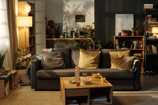 Spacious living room of modern flat with couch and square wooden table with snacks, drinks and board game