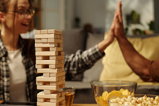 Focus on tower built up on table standing against two happy youthful friends giving one another high five