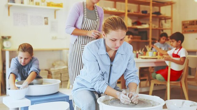 Pleased underage attendees of pottery circle working at throwing-wheel with female instructor