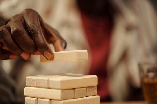 Hand of young African American man putting wooden block on top of tower while playing leisure game