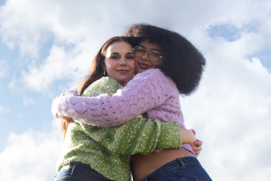 Two friends hugging outdoors under a bright sky