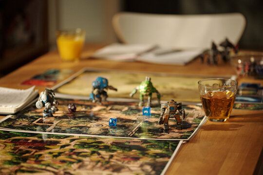 Glass of juice standing n wooden table next to board game pictures with plastic toy warriors and blue dice cubes