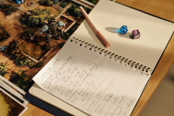 Open notepad with written tabletop game instructions, pen and two cube dices on its pages on table