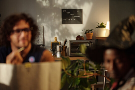 Focus on poster with lifestyle slogan hanging on wall of domestic kitchen with friends playing board game