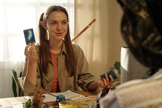 Smiling girl demonstrating game card with ball lightning to another participant of tabletop entertainment