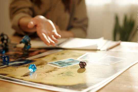 Two dice cubes on picture of board game with cards and toy warriors against hand of female player