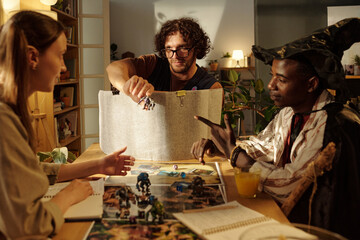 Young man in eyeglasses passing toy warrior to female participant of tabletop game during play