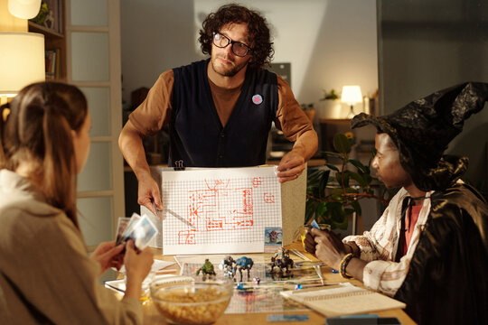 Serious young man pointing at board game sketch while explaining rules to participants during play