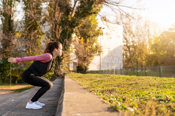 Active woman performing jump exercise in city park.