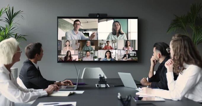 Diverse businesspeople, group of professionals take part in videoconference meeting, gathered together to solve business-related matters, listening participants making speech seen on tv screen view
