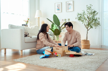 Couple Smiling While Carrying Plants and Baskets in a Sunlit Living Room Filled With Greenery