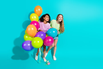 Two cheerful women with colorful balloons posing against a vibrant turquoise background, celebrating together in a stylish and playful summer scenario.