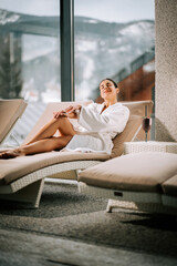 Woman in a white robe enjoys a relaxing moment with a cocktail while lounging in a spa with a mountain view