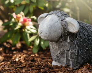 Stone sheep in a garden in front of a rhododendron shrub